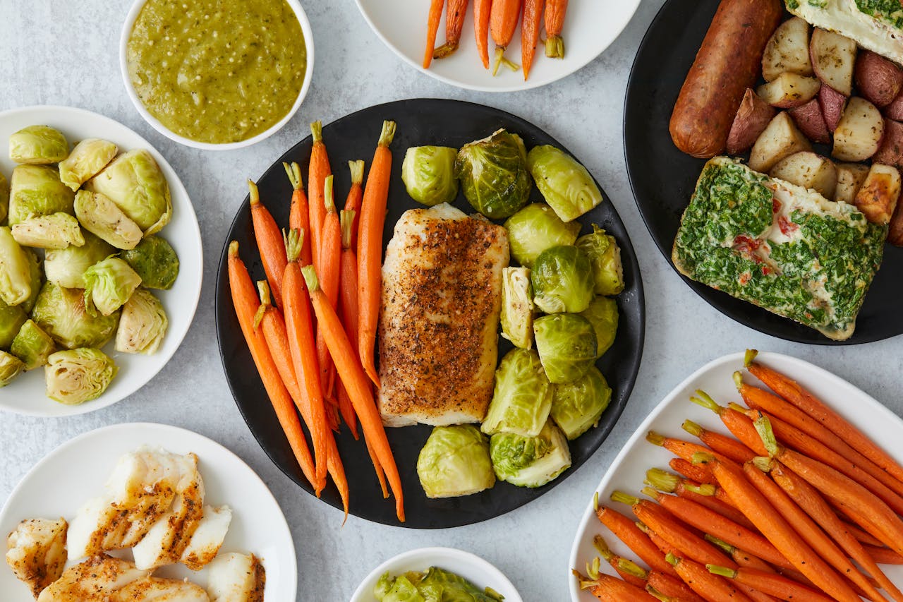Top view of a healthy meal with carrots, fish, and brussels sprouts on plates.